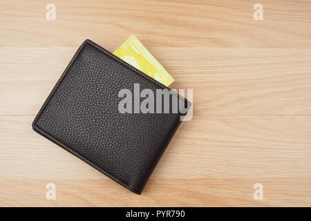 Yellow condoms in black wallet on wooden table background Stock Photo