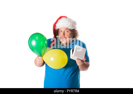 Funny fat man in Santa hat with balloons and gifts. Christmas and presents. Emotions Stock Photo