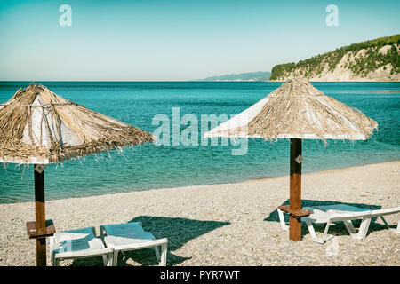 Beach umbrellas and sun beds on the ocean. Vacation and travel to different countries Stock Photo