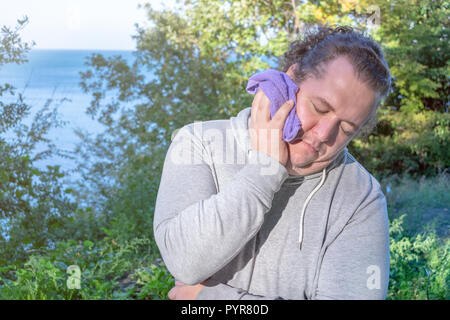 Fat man wipes his face with a towel standing on the ocean Stock Photo