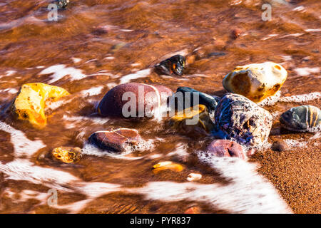 Highly coloured pebbles on a sandy beach in Devon, UK. Stock Photo