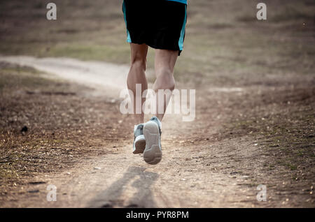 Back view of sport man with ripped athletic and muscular legs running off road in nature at autumn sunset in jogging training workout at countryside i Stock Photo