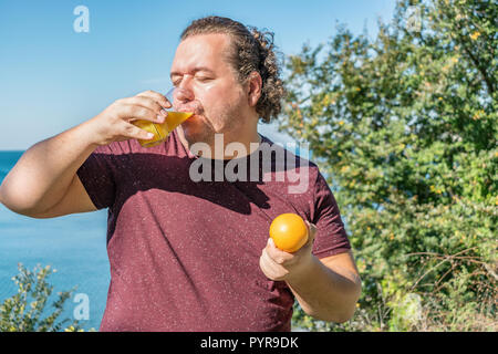 Funny fat man on the ocean drinking juice and eating fruits Stock Photo