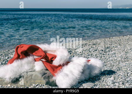 Santa Claus clothing and hat lies on a large stone on the seashore Stock Photo