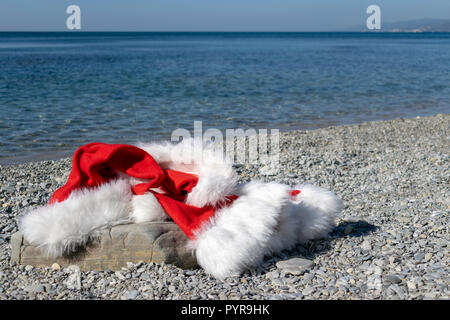 Santa Claus clothing and hat lies on a large stone on the seashore Stock Photo