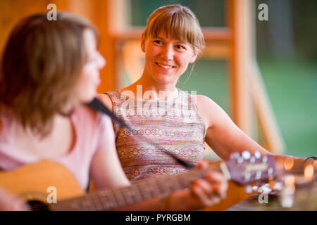 Woman playing guitar for friend at dinner table Stock Photo