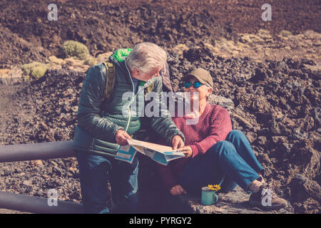 couple adult senior man and woman trekker explorer during a rest over the mountains drinking a tea or coffee and looking at the paper map to choose th Stock Photo