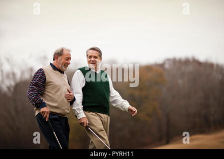 Two men carrying golf clubs walking and talking. Stock Photo