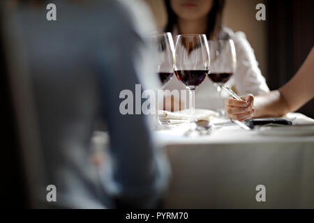 Three colleagues brainstorming while sitting around a table with three wine glasses. Stock Photo