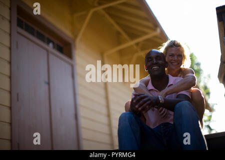 Mid-adult woman hugging her husband while sitting on steps outside. Stock Photo