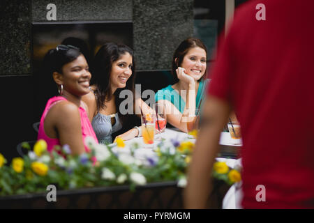 Three smiling young women sitting together at an outdoor cafe. Stock Photo