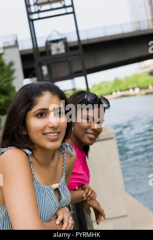 Two young woman leaning on the railing of a bridge near an inner city river. Stock Photo