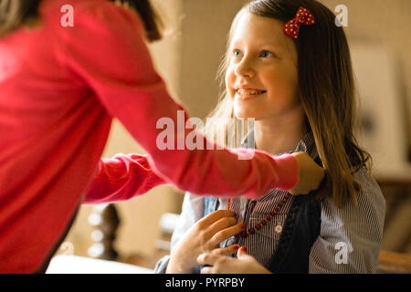 Young girl smiles as a friend leans over to place a necklace around her neck. Stock Photo