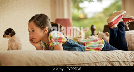 Young girl daydreaming while lying on her bed next to a puppy. Stock Photo