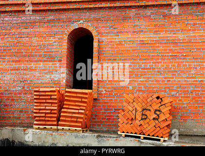 Red bricks on pallets near the wall of the building under construction Stock Photo