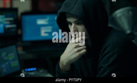 Young hacker with a hoodie thinking with hand on chin and working with computers, technology and cybercrime concept Stock Photo