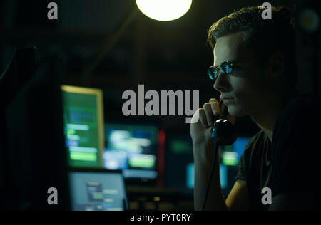 Hacker with sunglasses holding a telephone receiver and computer screens, coding and system hacking concept Stock Photo