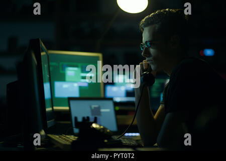 Hacker with sunglasses holding a telephone receiver and computer screens, coding and system hacking concept Stock Photo