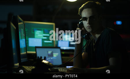 Hacker with sunglasses holding a telephone receiver and computer screens, coding and system hacking concept Stock Photo