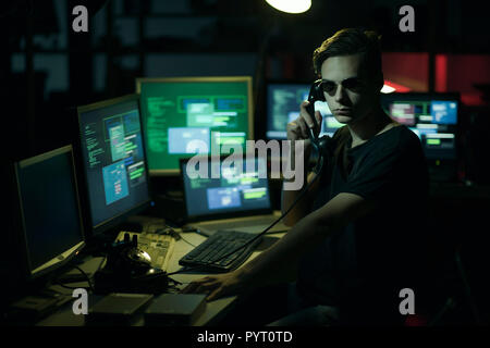 Hacker with sunglasses holding a telephone receiver and computer screens, coding and system hacking concept Stock Photo