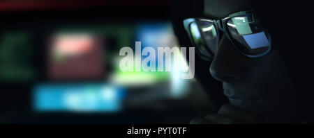 Nerd hacker with glasses working with a computer in the dark, cybersecurity concept Stock Photo