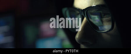 Nerd hacker with glasses working with a computer in the dark, cybersecurity concept Stock Photo