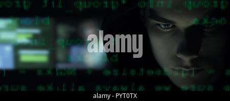 Cool young hacker with hoodie posing in the dark and programming code, cyber security and development concept Stock Photo