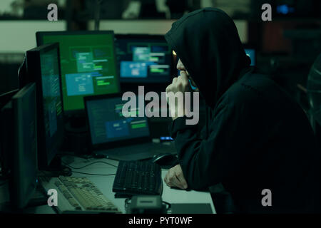 Young hacker with a hoodie thinking with hand on chin and working with computers, technology and cybercrime concept Stock Photo