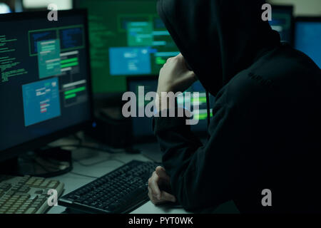Young hacker with a hoodie thinking with hand on chin and working with computers, technology and cybercrime concept Stock Photo