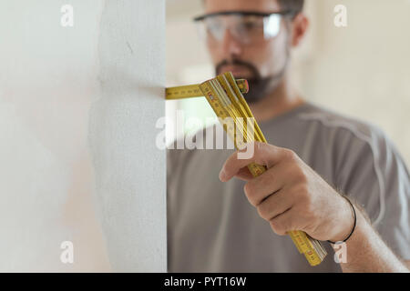 Man measuring a wall using a folding ruler: home renovation and construction concept Stock Photo