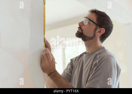 Man measuring a wall using a folding ruler: home renovation and construction concept Stock Photo