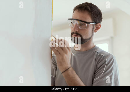 Man measuring a wall using a folding ruler: home renovation and construction concept Stock Photo