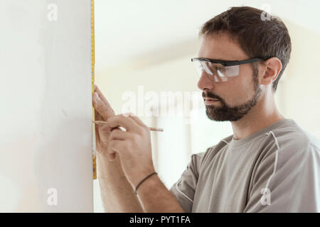 Man measuring a wall using a folding ruler: home renovation and construction concept Stock Photo