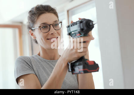Young smiling woman using a drill, home renovation and DIY concept Stock Photo