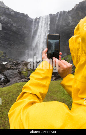 Tourist snaps photos with smartphone, Fossa waterfall, Streymoy island, Faroe Islands, Denmark Stock Photo