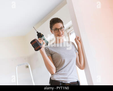 Professional repairwoman with tool belt doing a home renovation, she is posing and holding a drill Stock Photo