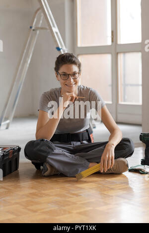 Attractive smiling woman working on a home renovation, she is sitting on the floor with tools and posing, house renovation concept Stock Photo