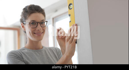 Young woman working with a spirit level and checking the surface of a wall, home renovation and construction concept Stock Photo