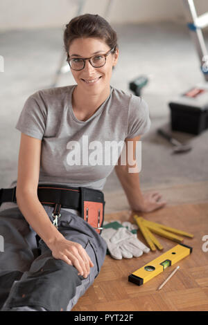 Attractive smiling woman renovating her house, she is sitting on the floor with tools and posing, home makeover concept Stock Photo