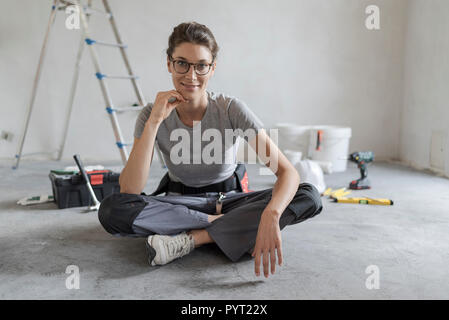 Attractive smiling woman renovating her house, she is sitting on the floor with tools and posing, home makeover concept Stock Photo