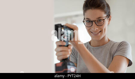 Young smiling woman using a drill, home renovation and DIY concept Stock Photo