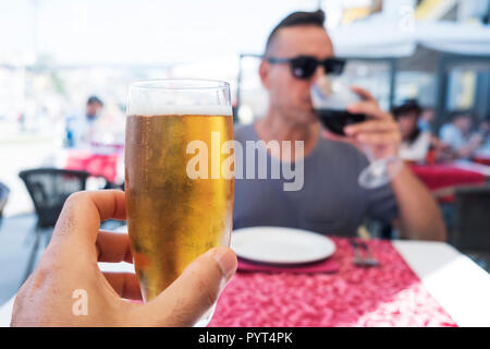 closeup of a caucasian man with a glass of refreshing beer in his hand and a young caucasian man drinking a glass of red wine, sitting both at the sam Stock Photo