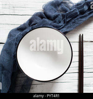 high angle view of a white ceramic bowl and a pair of black chopsticks placed on a white rustic wooden table Stock Photo