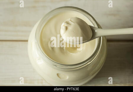Mayonnaise in a glass jar with a spoon on white wooden boards. Stock Photo