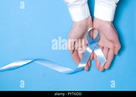 The symbol of men affected by prostate cancer is a light blue ribbon. A tape in the hands of a man on a blue background. Copy space. Stock Photo