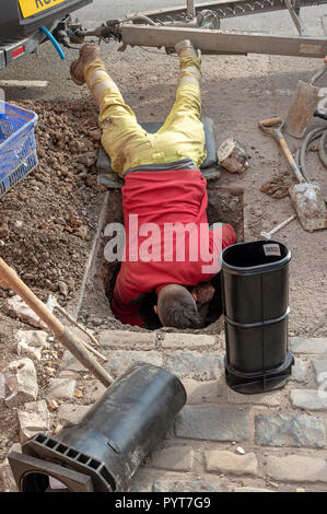 Installing a new water meter in the road. UK. Man leaning into a hole to make the installation Stock Photo