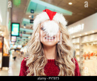 Pretty fashion model woman in Santa hat having fun on shopping mall background. Christmas or New Year sale and offer concept Stock Photo