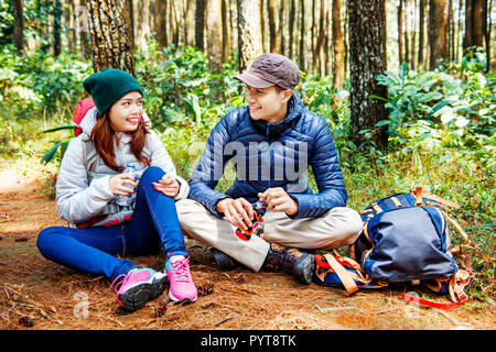 Smiling asian couple hikers take a rest while drink a water on the forest Stock Photo
