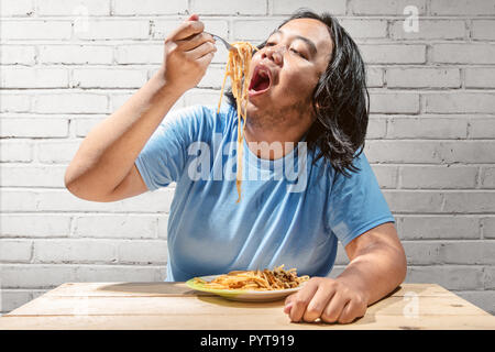 Asian fat man meal the fast food spaghetti at home. Fat man diet concept Stock Photo