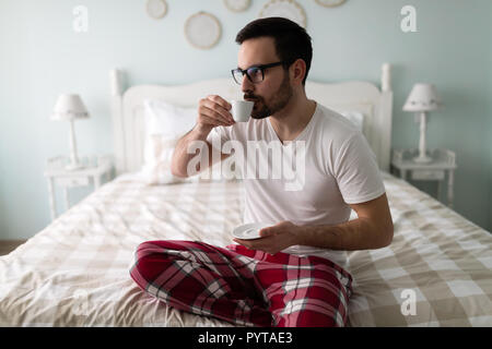 Young handsome man drinking coffee on his bed Stock Photo